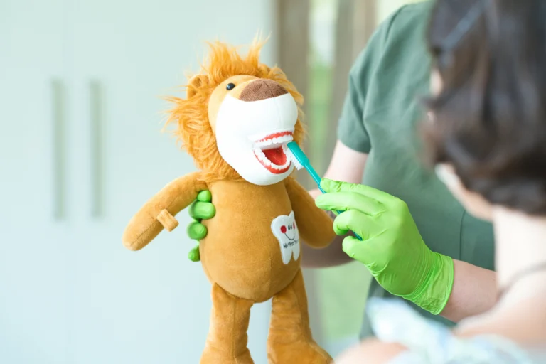 Eine Mitarbeiterin hält eine Löwen-Handpuppe und eine Zahnbürste zur Zahnputzübung.