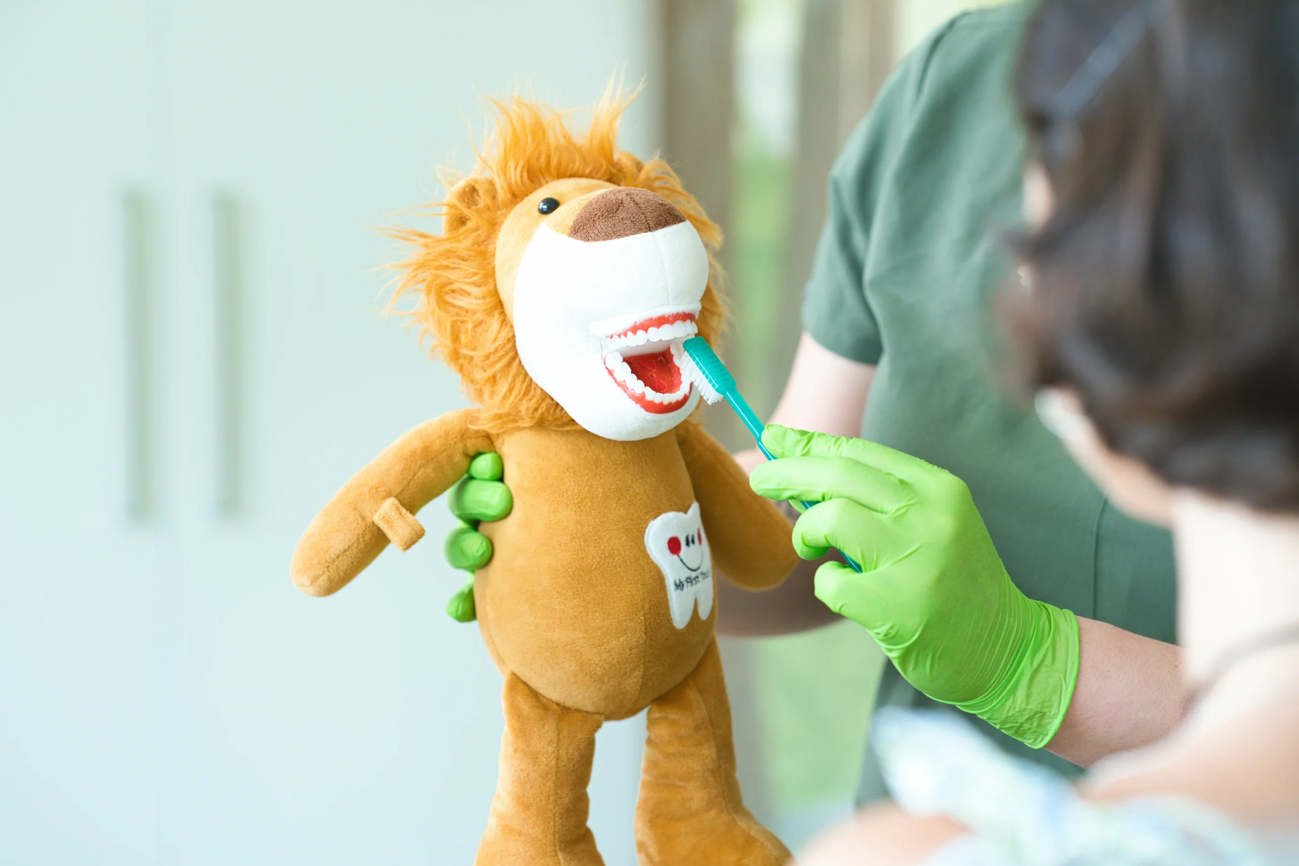 Eine Mitarbeiterin hält eine Löwen-Handpuppe und eine Zahnbürste zur Zahnputzübung.