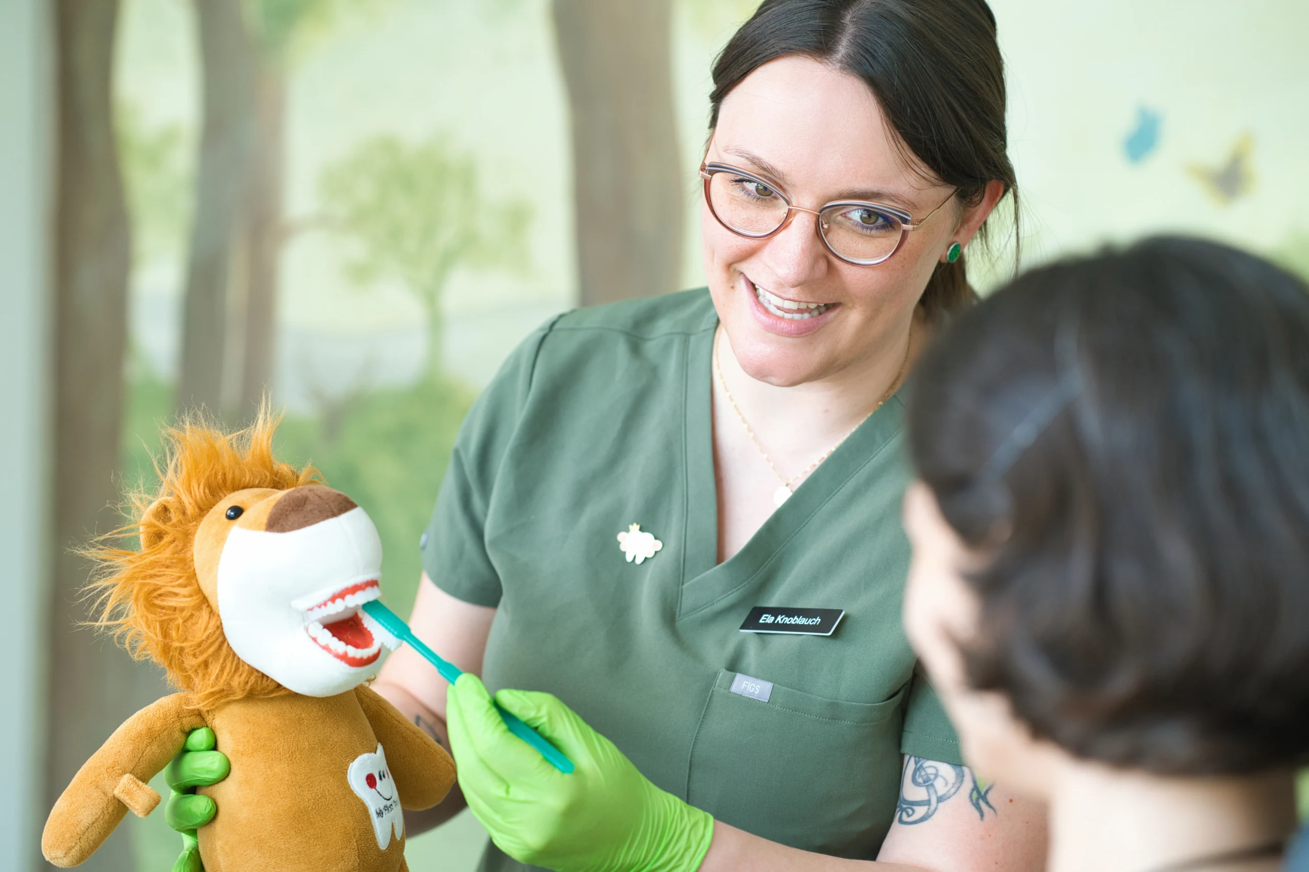 Eine Mitarbeiterin erklärt einem Kind das Zähneputzen mit einer Löwen-Handpuppe.