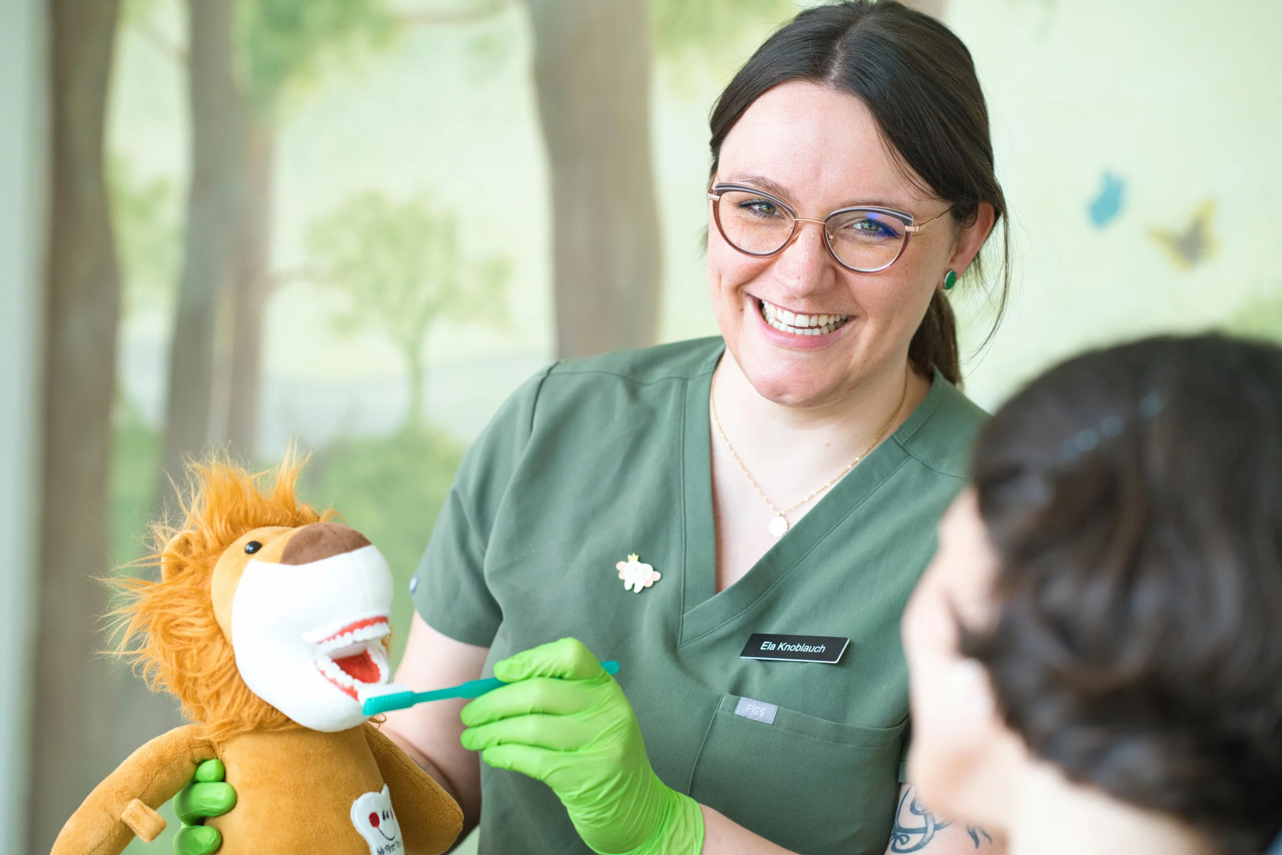 Eine Mitarbeiterin erklärt einem Kind das Zähneputzen mit einer Löwen-Handpuppe.